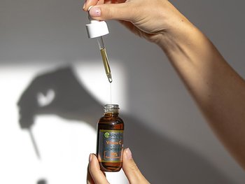 Eine Hand hält eine Pipette über einer Flasche Vitamin C Serum