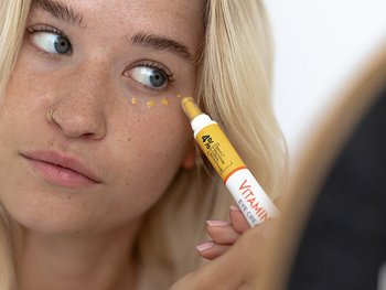Eine junge Frau trägt eine Vitamin C Glow Booster Anti-Müdigkeits Augencreme auf ihre Augenpartie auf