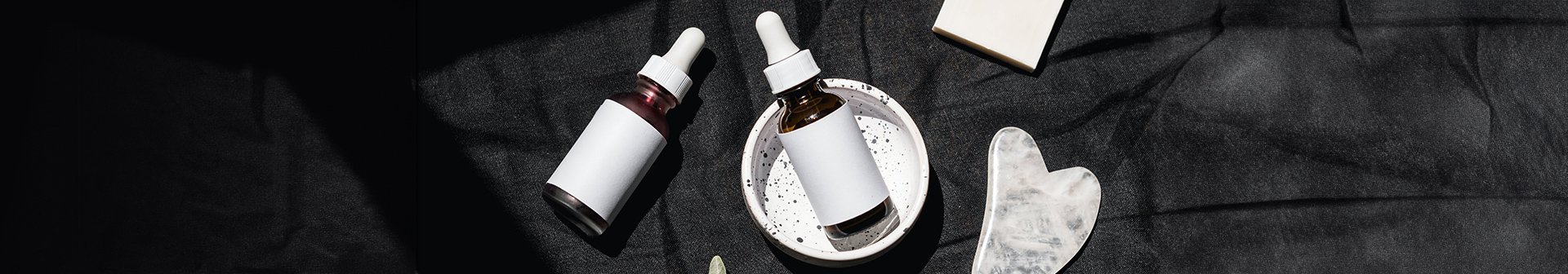 Stillleben mit zwei Ampullen, einem Olivenzweig und einer weißen Schale auf dunklem Untergrund