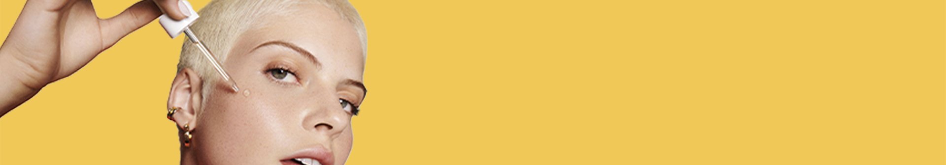 Ein junge Frau mit blonden kurzen Haaren trägt auf ihre Wange Vitamin C Serum mit Pinzette auf