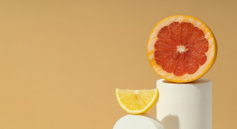 Eine aufgeschnittene Orange und ein Stück einer Zitrone auf zwei weißen Sockeln