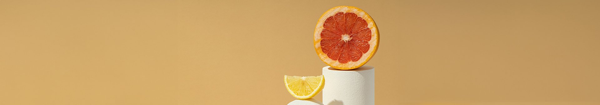 Eine aufgeschnittene Orange und ein Stück einer Zitrone auf zwei weißen Sockeln