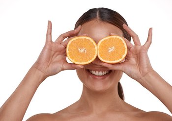 Eine junge Frau hält sich zwei halbe Orangen vor ihre Augen