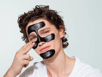 Mann trägt schwarze Peelingmaske auf sein Gesicht auf