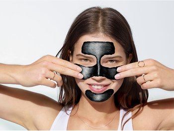 Lächelnde Frau trägt schwarze Peelingmaske auf ihr Gesicht auf