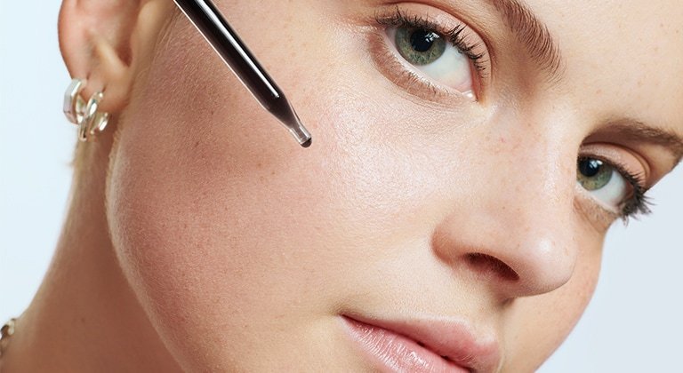 Frau trägt Serum aus einer Pipette auf ihre Wange auf