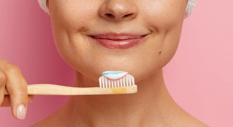 Eine junge Frau hält eine Zahnbürste mit Zahnpasta vor ihrem Gesicht