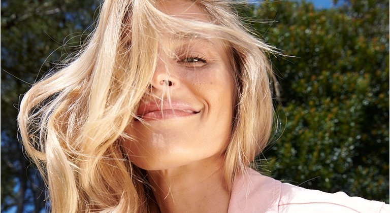Eine junge Frau mit langen blonden Haaren lächelt in der Sonne