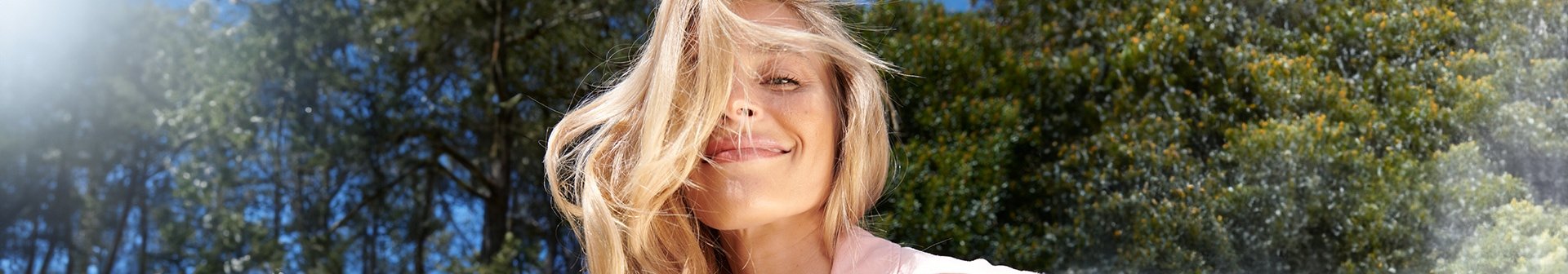 Eine junge Frau mit langen blonden Haaren lächelt in der Sonne