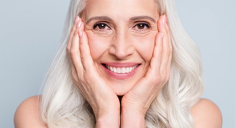 Frau mit langen grauen Haaren, lächelnd, ihr Gesicht auf ihre Hände gestützt