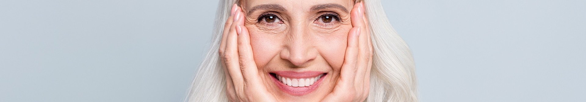 Frau mit langen grauen Haaren, lächelnd, ihr Gesicht auf ihre Hände gestützt