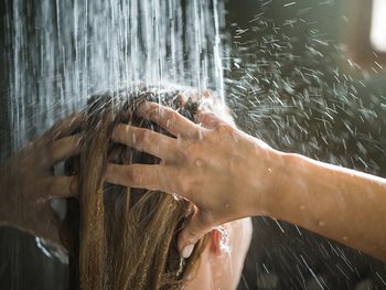 Blonde Frau unter der Dusche beim Haare waschen