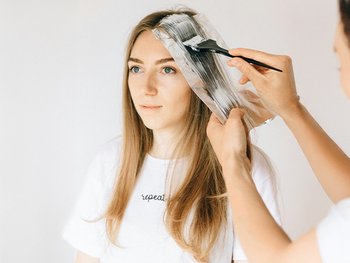 Eine blonde Haartönung wird auf die langen dunkelblonden Haare einer Frau aufgetragen