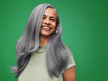 Eine Frau mit langen silbergrauen Haaren vor grünem Hintergrund