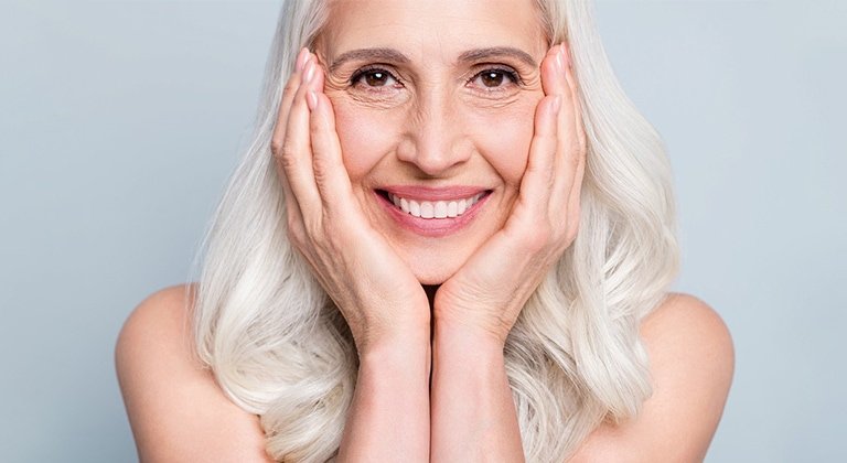 Eine lächelnde Frau mit langen grauen Haaren stützt ihr Gesicht auf ihre Hände