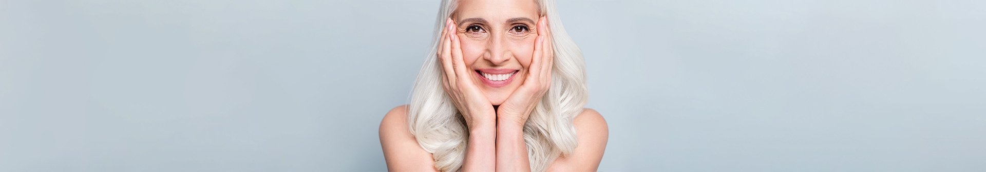 Eine lächelnde Frau mit langen grauen Haaren stützt ihr Gesicht auf ihre Hände
