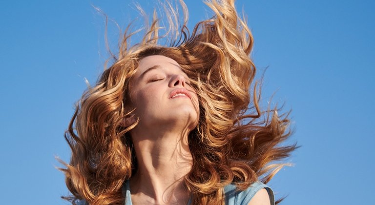 Eine junge Frau mit wallendem blonden Haaren lässt sich die Sonne auf ihr Gesicht scheinen