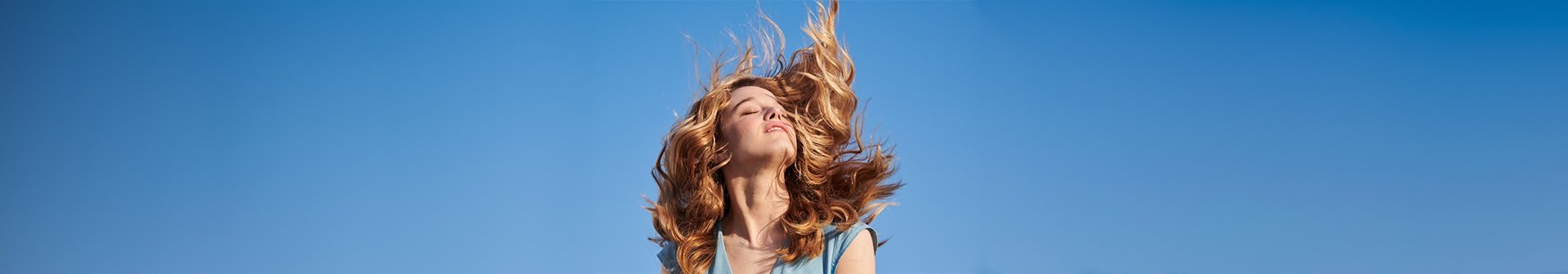 Eine junge Frau mit wallendem blonden Haaren lässt sich die Sonne auf ihr Gesicht scheinen