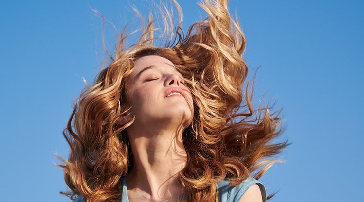 Eine junge Frau mit wallendem blonden Haaren lässt sich die Sonne auf ihr Gesicht scheinen