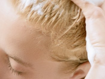 Junge Frau trägt ein Shampoo auf ihre blonden Haare auf