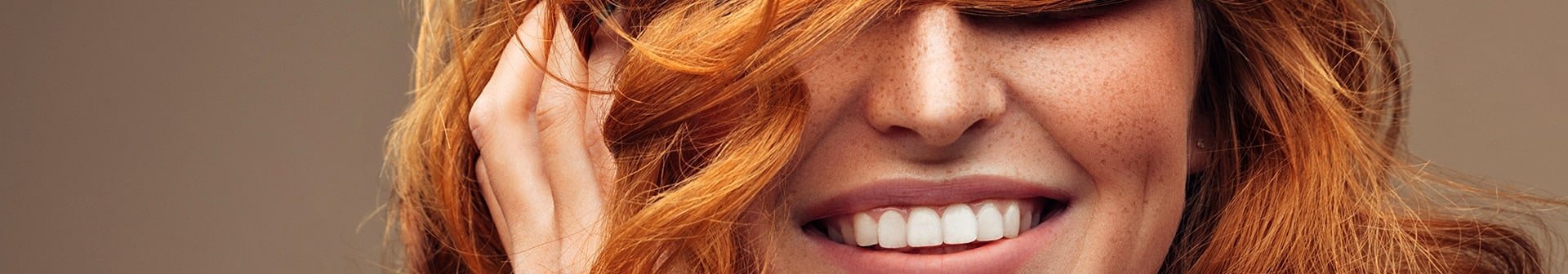 Lächelnde Frau hält sich ihre langen, roten Haare vor die Augen