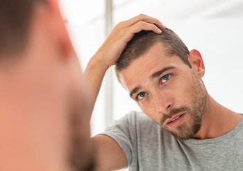 Mann mit kurzen dunklen Haaren, der seinen Kopf seitlich hält und sich im Spiegel betrachtet