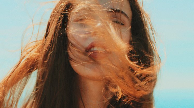 Wind weht einer Frau ihr rotbraunes Haar ins Gesicht