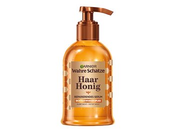 Haar Honig Reparierende Haarserum in der Hand einer Frau vor einem orangebraunem Hintergrund