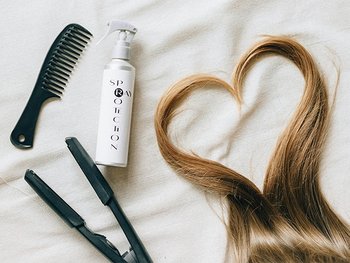 Zwei blonde Haarsträhnen, die ein Herz bilden neben verschiedenen Styling-Produkten