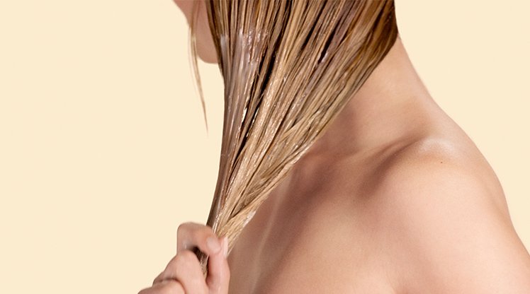 Eine Frau fasst ihre langen blonden nassen Haare zusammen