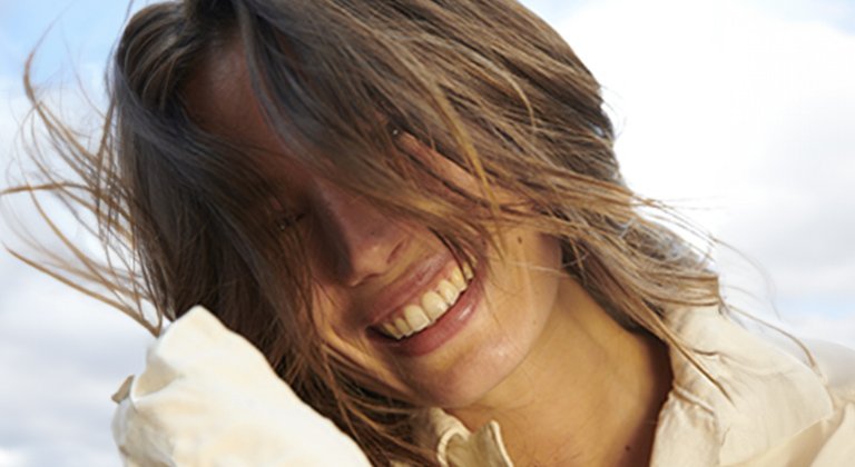 Eine lächelnde junge Frau wehen die Haare vor ihr Gesicht