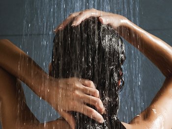 Hinterkopf einer brünetten Frau, die sich unter die Dusche die Haare wäscht