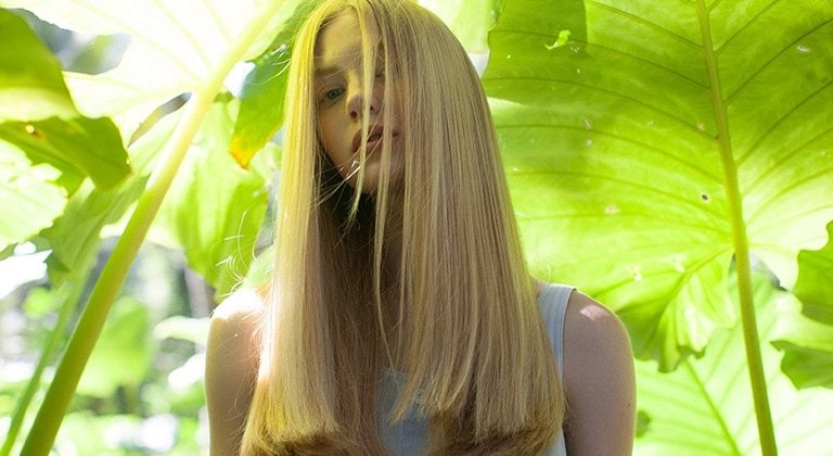Blonde Frau vor tropischen Pflanzen