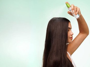 Frau pflegt ihr langes glattes Haar mit einem Keratin-Spray
