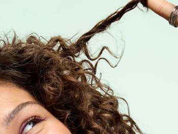 Frau spielt mit einer lockigen Haarsträhne, die mit Keratin gepflegt werden kann