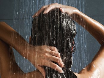 Hinterkopf einer brünetten Frau, die ihre Haare unter der Dusche wäscht