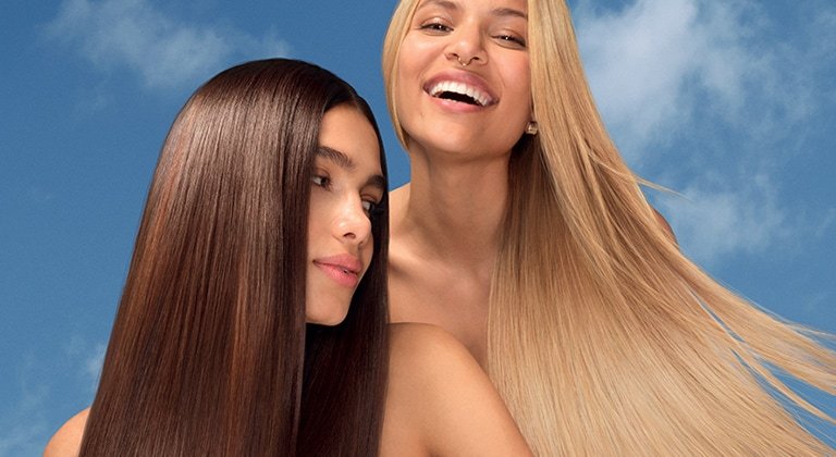 Zwei lächelnde junge Frauen mit langen Haaren vor blauen Himmel