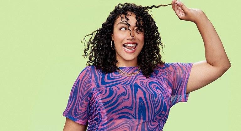 Eine lächelnde junge Frau zieht an einer Strähne ihrer lockigen Haare