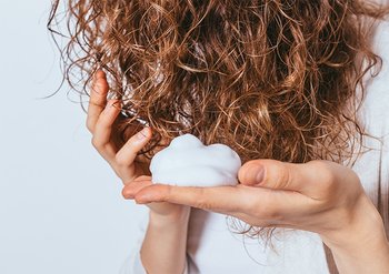 Frau hält sich naturkrauses Haar und hat Schaumfestiger auf der Hand
