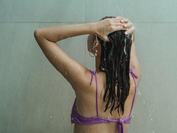 Brünette Frau, die sich die Haare wäscht in der Dusche