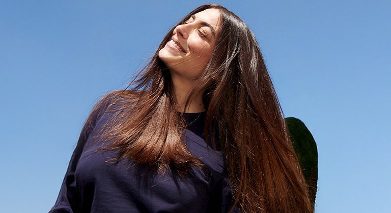 Dunkelhaarige Frau mit langen Haaren die lächelnd in den Himmel schaut