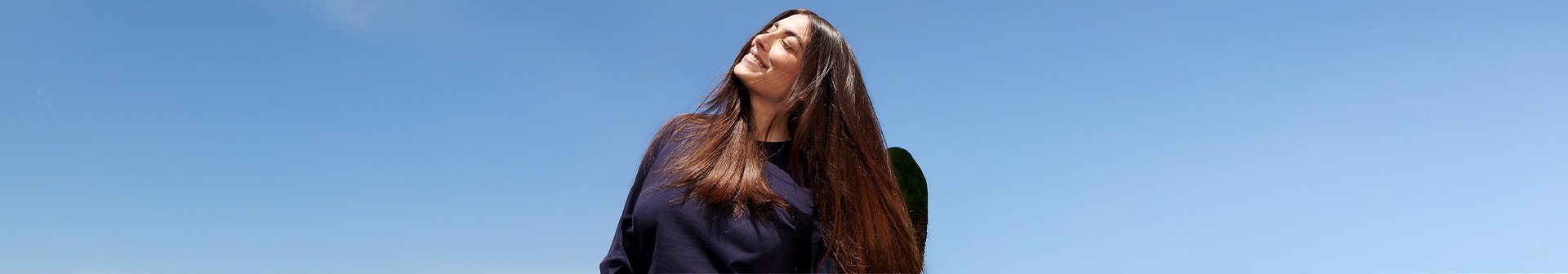 Dunkelhaarige Frau mit langen Haaren die lächelnd in den Himmel schaut