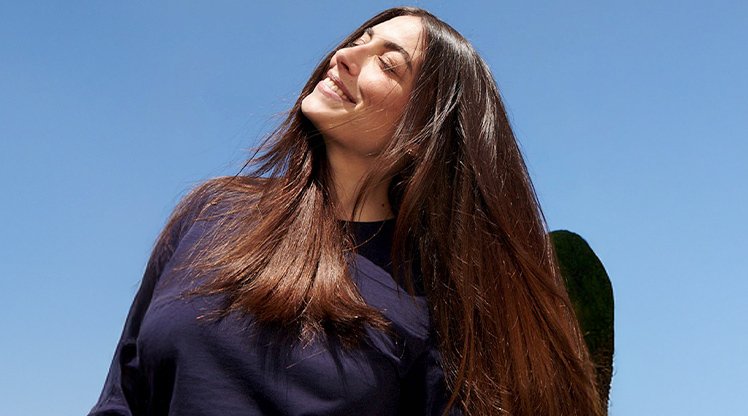 Dunkelhaarige Frau mit langen Haaren die lächelnd in den Himmel schaut