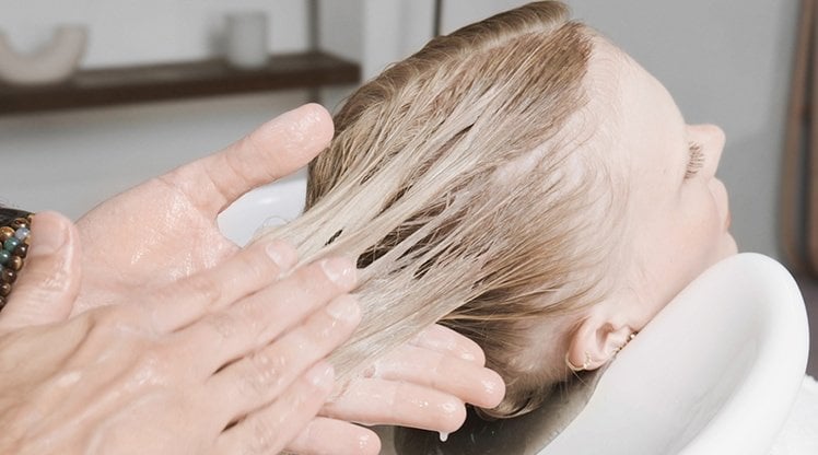 Blonde Frau, der Conditioner in ihr nasses Haar gegeben wird.