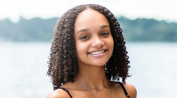 Gesicht einer lächelnden jungen Frau mit dunkelbraunen Naturlocken