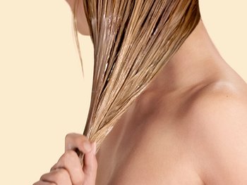 Blonde Frau, die Conditioner in ihre nassen Haare aufträgt