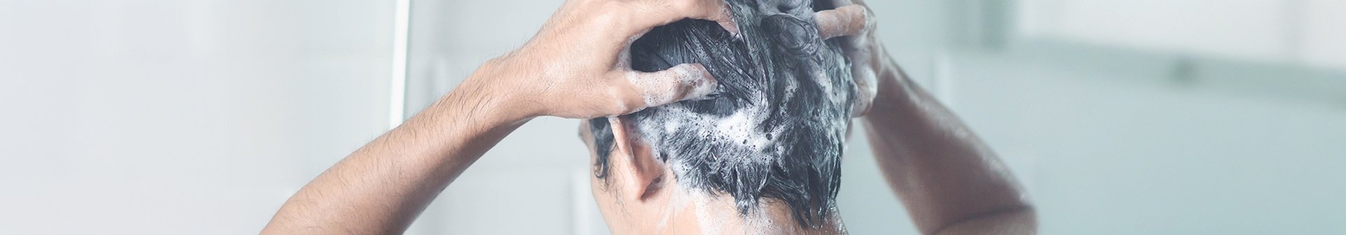 Eine Person steht unter der Dusche und massiert Shampoo in ihre nassen Haare ein, während Wasser herunterläuft