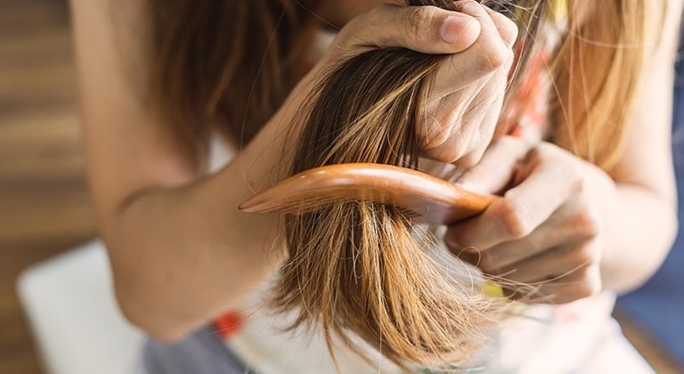 Eine Frau haelt ihre langen Haare fest und kaemmt die Spitzen mit einem Kamm
