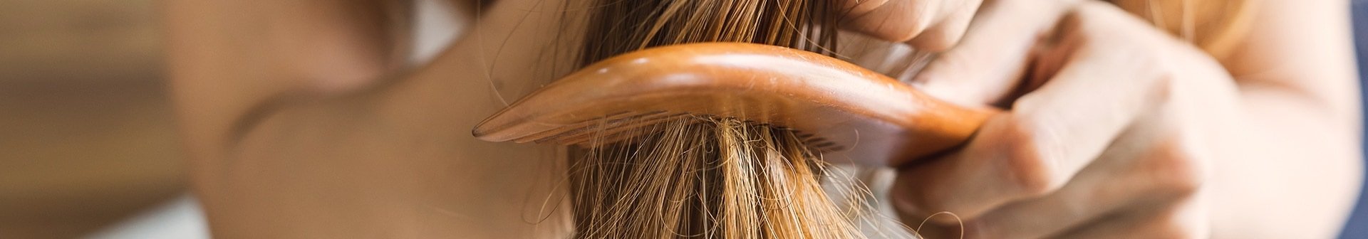 Eine Frau haelt ihre langen Haare fest und kaemmt die Spitzen mit einem Kamm