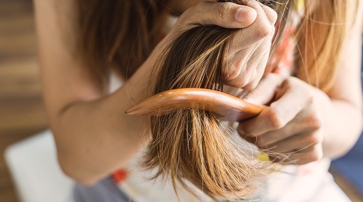 Eine Frau haelt ihre langen Haare fest und kaemmt die Spitzen mit einem Kamm